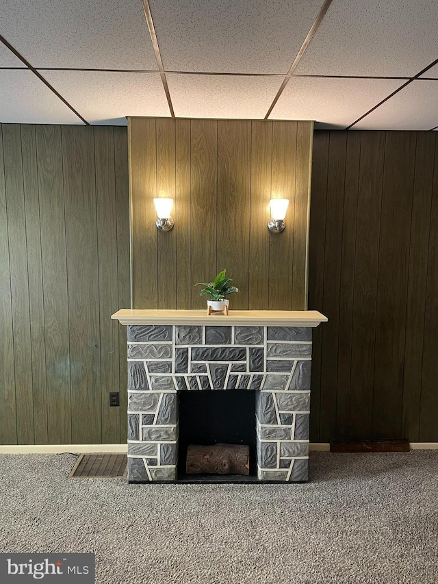 details with wooden walls, a paneled ceiling, carpet flooring, and a stone fireplace