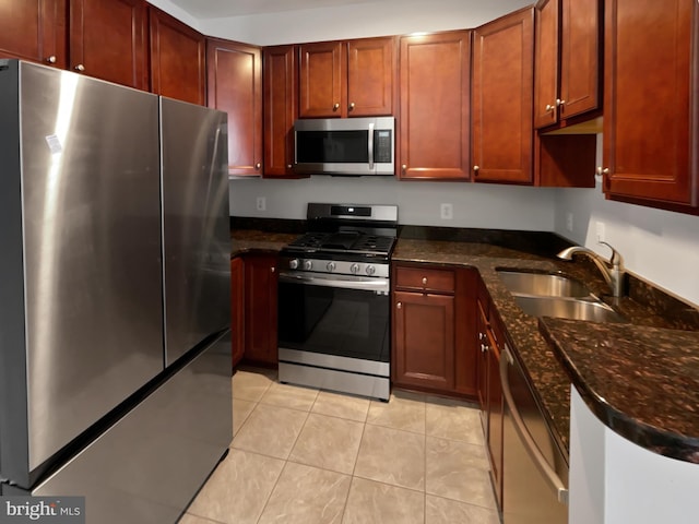 kitchen with light tile patterned floors, appliances with stainless steel finishes, dark stone counters, and a sink