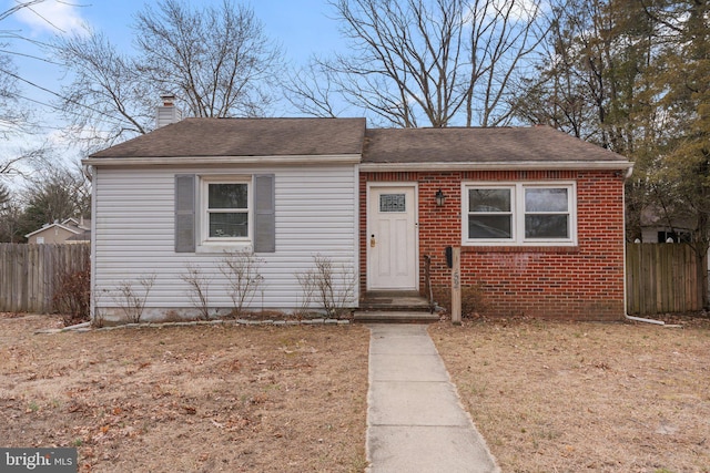 view of front facade featuring roof with shingles, brick siding, a chimney, and fence