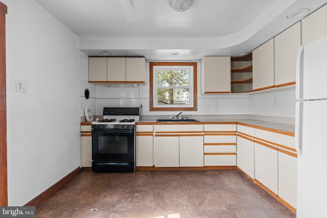 kitchen featuring open shelves, backsplash, freestanding refrigerator, a sink, and gas range