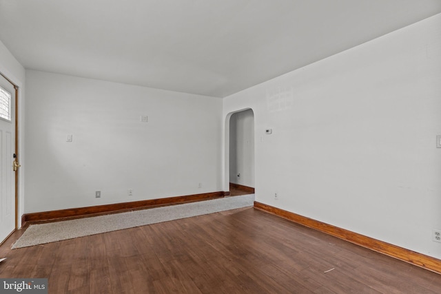 spare room with baseboards, arched walkways, and wood finished floors