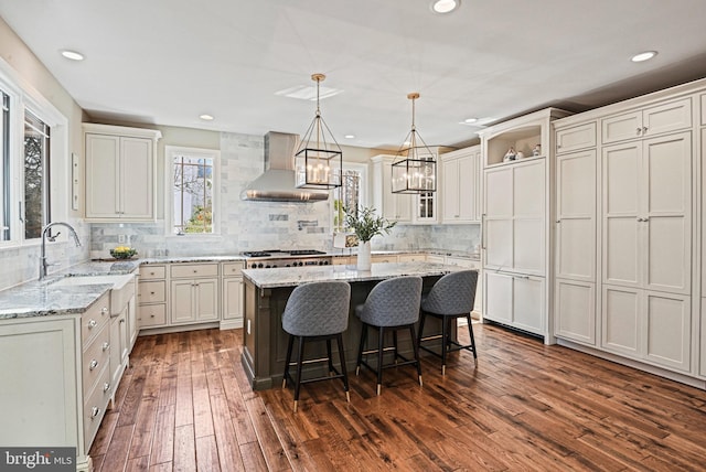 kitchen featuring dark wood finished floors, a sink, a kitchen bar, wall chimney range hood, and a center island