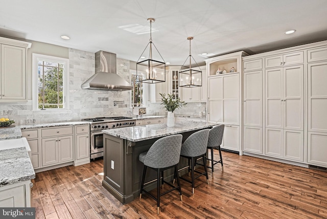 kitchen featuring a center island, range with two ovens, decorative backsplash, wood finished floors, and wall chimney exhaust hood