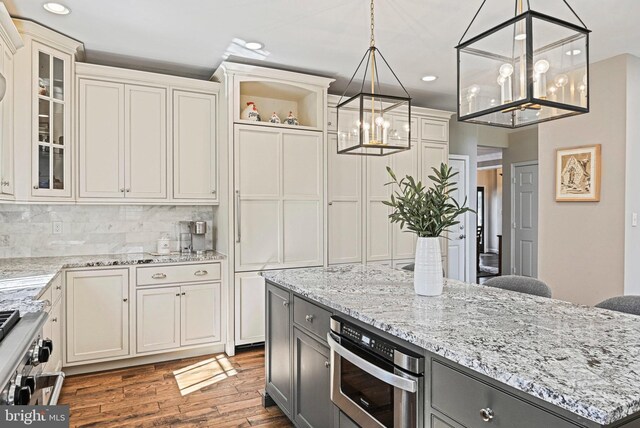 kitchen featuring gray cabinets, backsplash, wood finished floors, glass insert cabinets, and light stone countertops