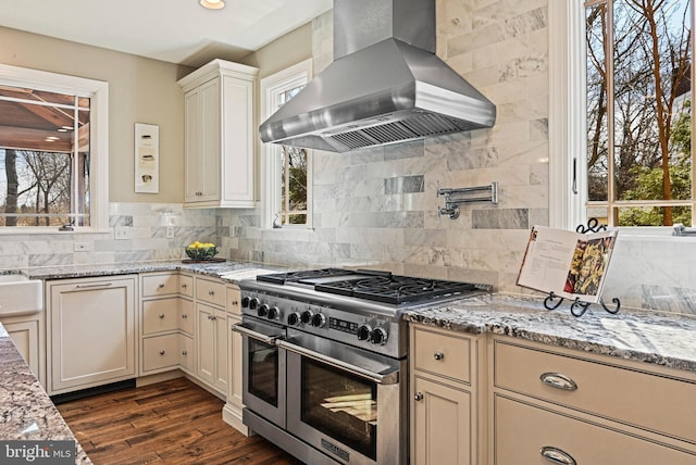 kitchen featuring light stone counters, decorative backsplash, range hood, and double oven range