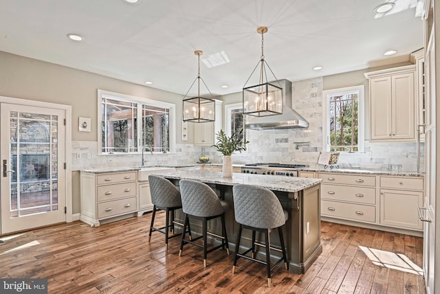 kitchen featuring light stone countertops, a kitchen island, hardwood / wood-style flooring, stainless steel gas stovetop, and wall chimney exhaust hood