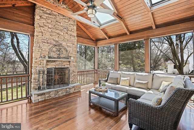 sunroom / solarium with vaulted ceiling with skylight, wooden ceiling, an outdoor stone fireplace, and a ceiling fan