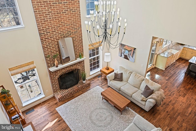 living area with dark wood-style floors, visible vents, a high ceiling, a fireplace, and a notable chandelier