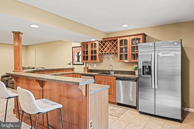 kitchen with glass insert cabinets, a breakfast bar, a peninsula, stainless steel appliances, and a sink