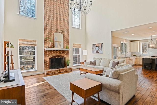 living area featuring a notable chandelier, a healthy amount of sunlight, a brick fireplace, and dark wood-type flooring