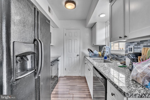 kitchen with tasteful backsplash, light stone countertops, light wood-style floors, black appliances, and a sink