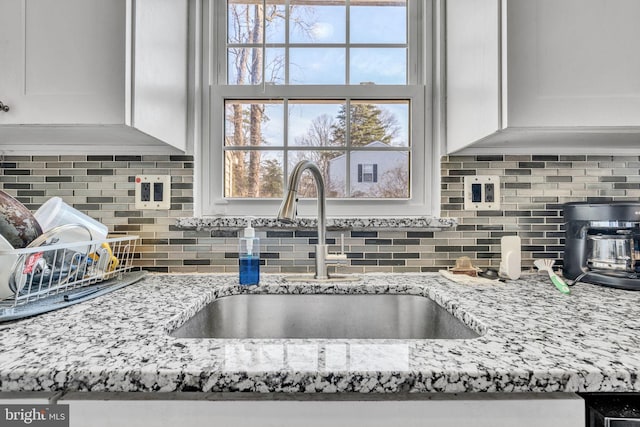 interior details with white cabinetry, light stone counters, tasteful backsplash, and a sink