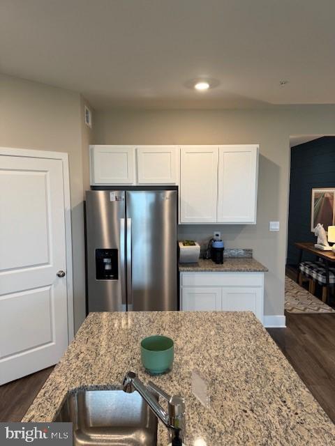 kitchen featuring light stone counters, dark wood finished floors, stainless steel refrigerator with ice dispenser, white cabinetry, and a sink