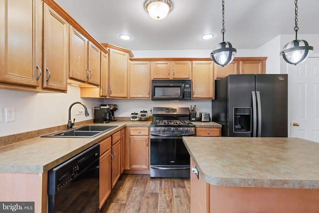 kitchen featuring light wood-style floors, light countertops, black appliances, pendant lighting, and a sink