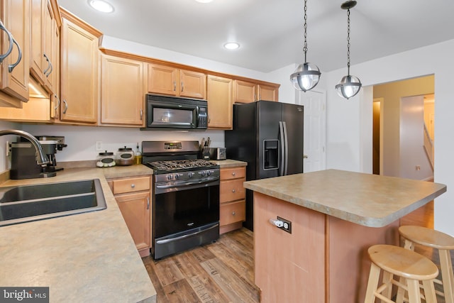 kitchen with a sink, light countertops, a center island, black appliances, and light wood finished floors