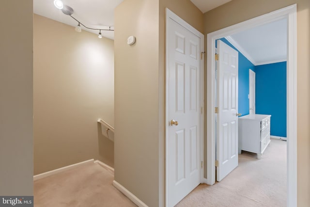 hall featuring baseboards, light colored carpet, track lighting, and an upstairs landing