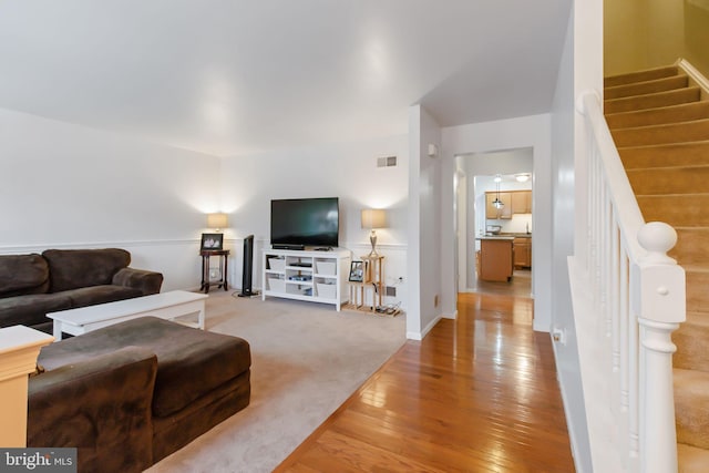 living area with light wood-type flooring, visible vents, light carpet, and stairway