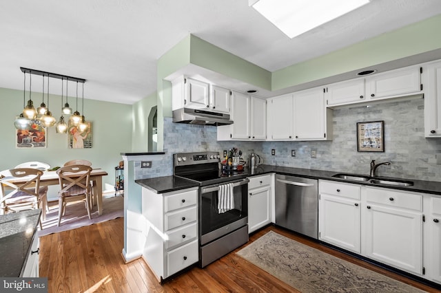 kitchen with under cabinet range hood, stainless steel appliances, dark countertops, and a sink