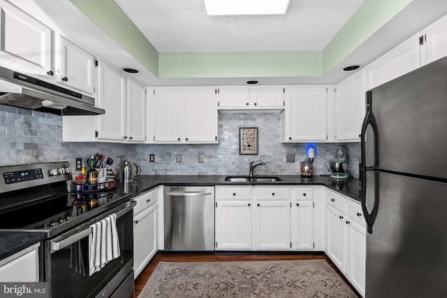 kitchen with dark countertops, under cabinet range hood, white cabinets, a sink, and stainless steel appliances