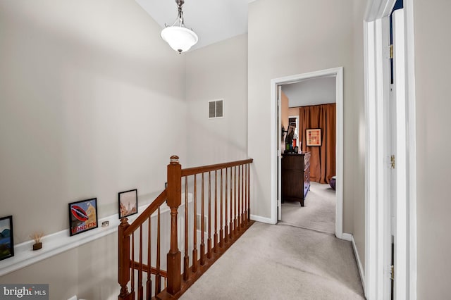 hall with carpet floors, baseboards, visible vents, and an upstairs landing