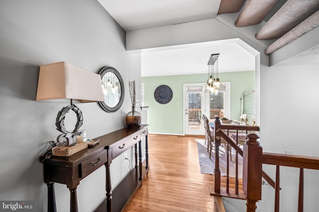 corridor with baseboards, light wood-type flooring, and a notable chandelier