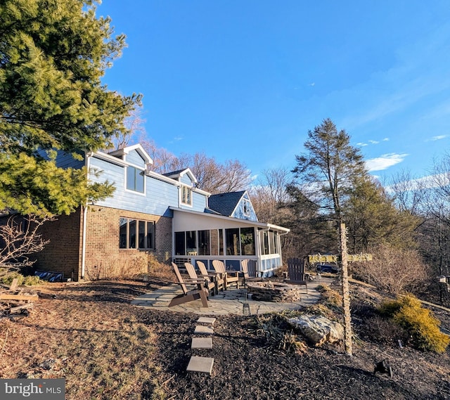 rear view of property featuring a sunroom, a patio area, and brick siding