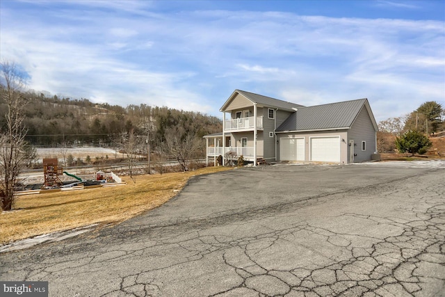 view of front facade with driveway, a balcony, metal roof, an attached garage, and a playground