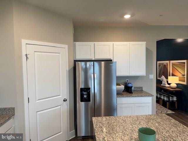 kitchen with stainless steel refrigerator with ice dispenser, white cabinetry, and light stone countertops