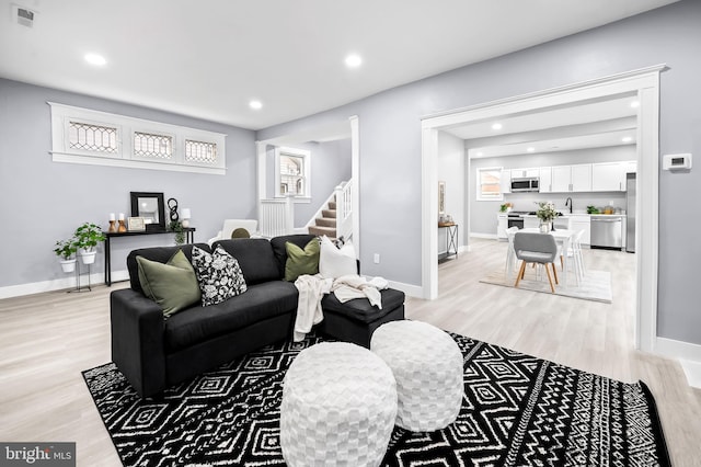 living room featuring light wood-type flooring, stairway, baseboards, and visible vents