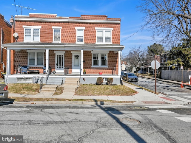 multi unit property featuring brick siding, a porch, and fence