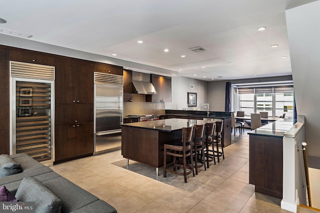 kitchen featuring visible vents, built in refrigerator, beverage cooler, a peninsula, and wall chimney exhaust hood