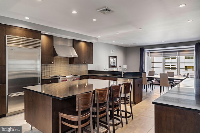 kitchen featuring built in fridge, light tile patterned floors, stove, a peninsula, and wall chimney exhaust hood