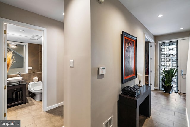 hallway featuring light tile patterned floors, recessed lighting, visible vents, a sink, and baseboards