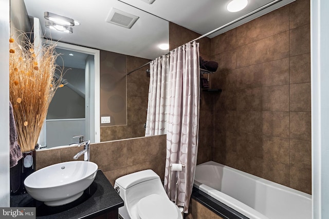 bathroom featuring visible vents, toilet, tiled shower / bath combo, vanity, and tile walls