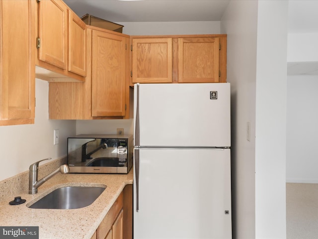 kitchen featuring light stone counters, stainless steel microwave, freestanding refrigerator, and a sink