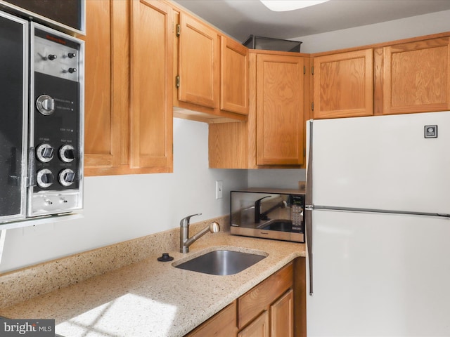 kitchen with stainless steel microwave, light stone countertops, freestanding refrigerator, and a sink