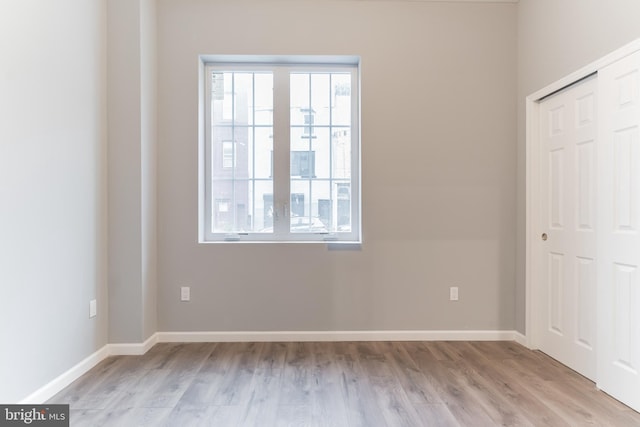 unfurnished bedroom featuring light wood finished floors, baseboards, and a closet