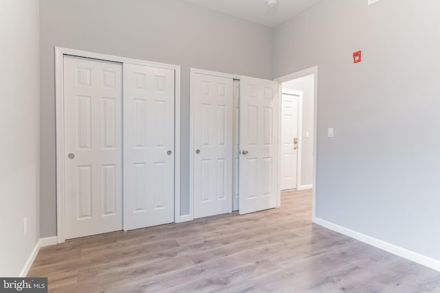 unfurnished bedroom featuring baseboards, two closets, and wood finished floors