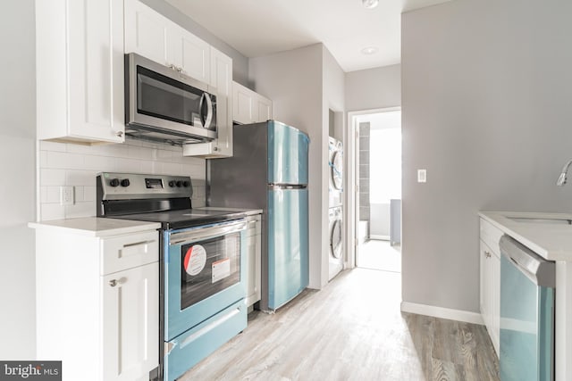 kitchen featuring tasteful backsplash, stacked washer / dryer, stainless steel appliances, white cabinetry, and a sink