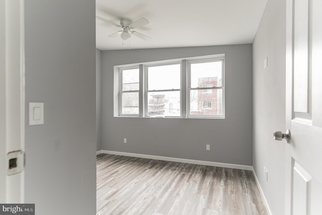 empty room with a healthy amount of sunlight, ceiling fan, baseboards, and wood finished floors