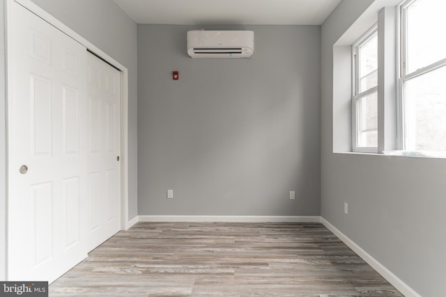 unfurnished bedroom with an AC wall unit, light wood-type flooring, and baseboards