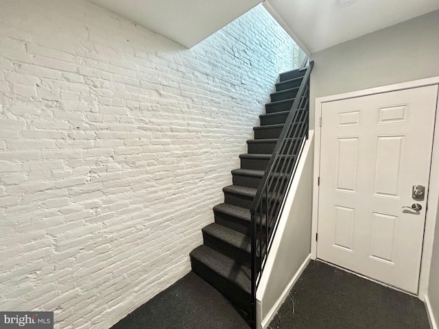 stairway featuring brick wall and baseboards