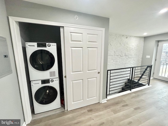 clothes washing area featuring laundry area, stacked washing maching and dryer, wood finished floors, and baseboards