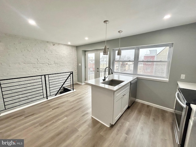 kitchen featuring light wood finished floors, white cabinets, appliances with stainless steel finishes, pendant lighting, and a sink