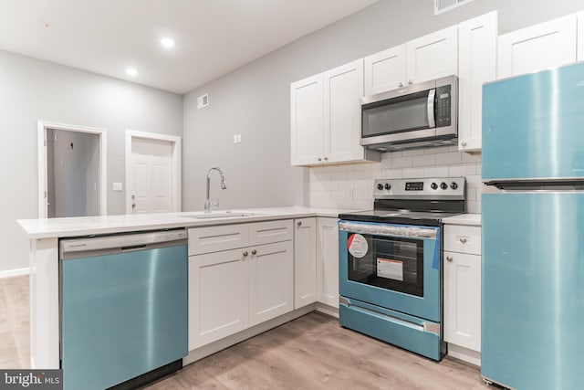 kitchen featuring stainless steel appliances, a peninsula, a sink, light wood-style floors, and decorative backsplash