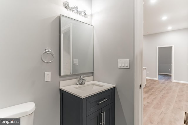 half bathroom with baseboards, toilet, wood finished floors, vanity, and recessed lighting