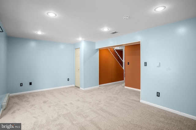 finished basement with visible vents, a baseboard heating unit, baseboards, stairway, and light colored carpet