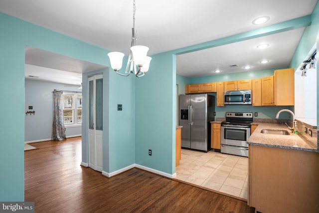 kitchen featuring pendant lighting, light stone counters, light wood-style floors, stainless steel appliances, and a sink