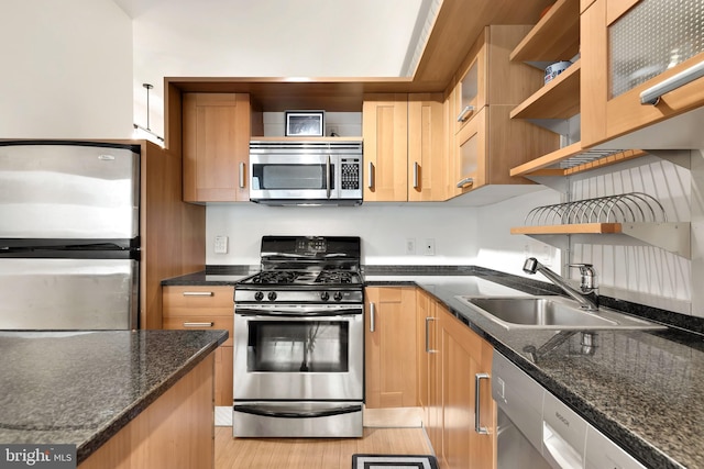 kitchen with stainless steel appliances, a sink, light wood-style floors, open shelves, and dark stone countertops