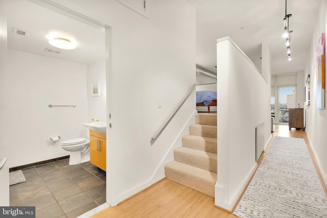 stairs with baseboards, visible vents, track lighting, and wood finished floors